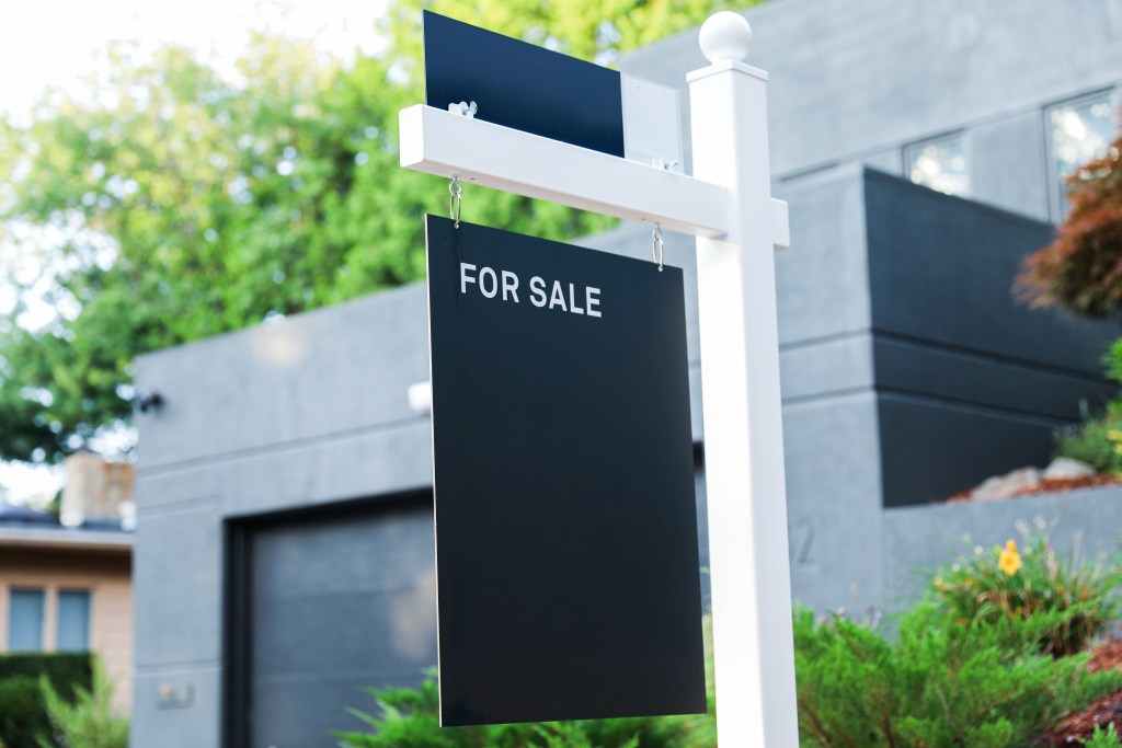 A 'For Sale' sign displayed in front of a modern residential building, surrounded by greenery.